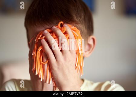 Jeune garçon couvrant son visage avec un jouet orange Banque D'Images