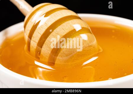 Miel d'abeille naturel liquide dans un bol en céramique blanc avec une cuillère en bois. Banque D'Images