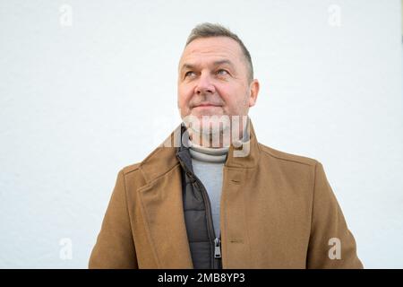 Portrait d'un homme d'âge moyen avec un sourire doux dans un manteau brun regardant vers le haut Banque D'Images