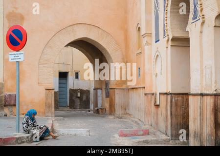 Fez, Maroc - porte originale de Bab Bou Jeloud dans la médina ancienne de Fes el Bali. Entrée médiévale simple et modeste. Le mendiant de la vieille femme est assis sur le trottoir. Banque D'Images