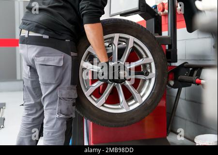 Vue latérale de la récolte mécanicien masculin méconnaissable en tenue décontractée et gants fixant la roue de voiture pendant le travail dans un garage moderne Banque D'Images