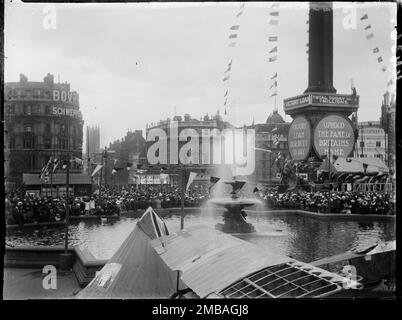 Trafalgar Square, St James, Westminster, City of Westminster, Greater London Authority, 1919. Une vue sur une fontaine de Trafalgar Square vers une grande foule de personnes rassemblées pour acheter des obligations de prêt de la victoire. Après la première Guerre mondiale, le gouvernement britannique était lourdement endetté et l'une des manières dont ils ont collecté de l'argent était de vendre des obligations de prêt et des certificats Victory au public. Lors de cet événement, des tentes ont été érigées à Trafalgar Square avec des banderoles et des slogans patriotiques attachés à la colonne de Nelson pour annoncer la vente des obligations. Cette photo fait partie d'un groupe que le photographe a pris à Trafalga Banque D'Images