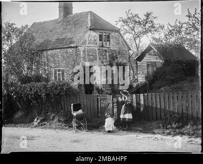 Grand et petit Kimble, Wycombe, Buckinghamshire, 1910. Deux enfants avec un pram, debout près de la porte du jardin à un cottage en briques non identifié dans Great Kimble ou Little Kimble. Banque D'Images