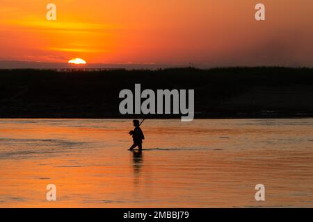 L'homme marche devant le soleil de Setting marche dans l'eau. Belle réflexion d'un homme traversant une rivière en face du soleil couchant - Myanmar Banque D'Images