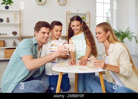 Une famille heureuse avec deux enfants joue des puzzles à la table assise sur le sol à la maison en week-end. Banque D'Images