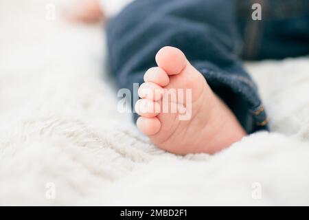 Un gros plan du pied d'un bébé sur une couverture floue portant un Jean. Banque D'Images