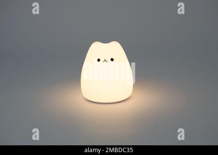 Lampe en forme de chat sur fond sombre. Jolie lampe de nuit en silicone en forme de chat sur fond blanc dans un espace sombre. Banque D'Images