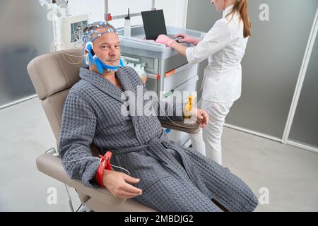 L'homme âgé est assis sur une chaise médicale avec des électrodes sur la tête Banque D'Images