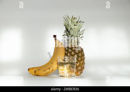 L'ananas et les bananes sont à côté d'un verre d'eau sur fond blanc, le régime et la nourriture végétaliens Banque D'Images