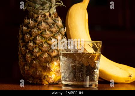 L'ananas et les bananes sont à côté d'un verre d'eau sur fond blanc, le régime et la nourriture végétaliens Banque D'Images