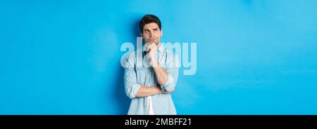 Image d'un homme barbu adulte de 25 ans, en pensant à quelque chose, en regardant dans le coin supérieur gauche et en réfléchissant des idées, debout sur fond bleu Banque D'Images