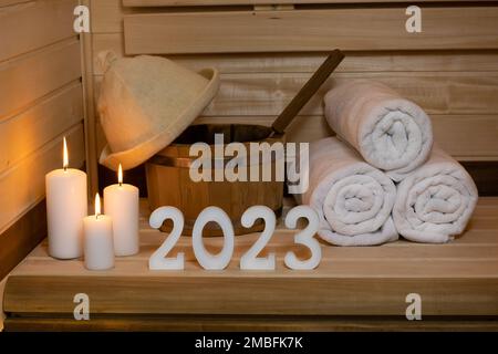 Sauna. Chiffres 2023 blanc en bois, bougies sont un chapeau éclairé, et une serviette. Banque D'Images