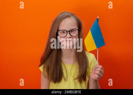 Une fille avec le syndrome de Down tient le drapeau de l'Ukraine. arrière-plan orange Banque D'Images