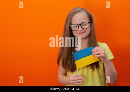 Une fille avec le syndrome de Down tient le drapeau de l'Ukraine. arrière-plan orange Banque D'Images