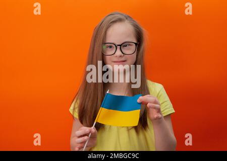 Une fille avec le syndrome de Down tient le drapeau de l'Ukraine. arrière-plan orange Banque D'Images