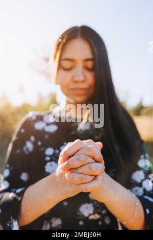 Jeune femme croyant personne avec les mains de prière au coucher du soleil dans le champ. Soumission à Dieu en prie. Banque D'Images