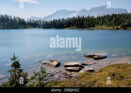 Vue depuis la côte est rocheuse du lac Larix, sur une rive ouest boisée, jusqu'à la montagne Monarch au loin Banque D'Images