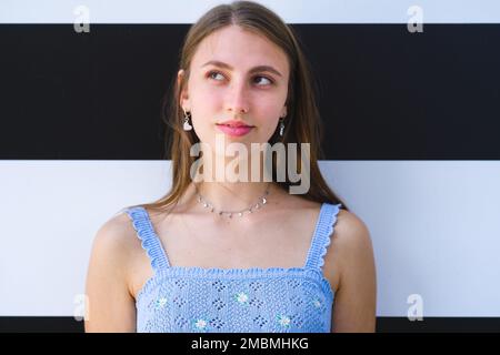 Gros plan d'une adolescente souriante debout devant le mur à rayures noires et blanches et regardant vers le haut et vers la droite Banque D'Images