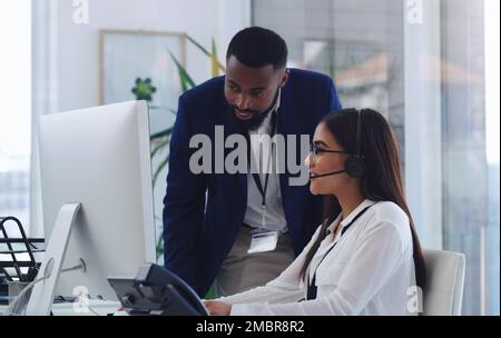 Permet de résoudre ce problème ensemble. un jeune homme d'affaires aidant un collègue dans un centre d'appels. Banque D'Images