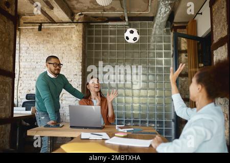 Jeunes collègues multiethniques divers jouant au football dans un bureau de coworking Banque D'Images