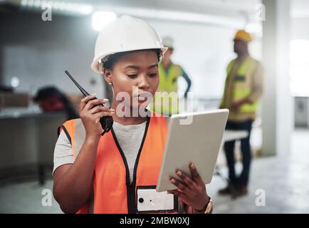 Excellence en construction. une jeune femme utilisant une tablette numérique et un talkie-walkie tout en travaillant sur un chantier de construction. Banque D'Images