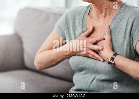 Protégez votre cœur. une femme âgée souffrant de douleurs à la poitrine tout en étant assise sur le canapé à la maison. Banque D'Images