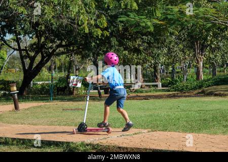 Portrait d'une petite fille active en scooter dans la rue dans un parc extérieur le jour d'été. Bonne fille asiatique portant un casque à cheval sur un scooter de coup de pied dans le Banque D'Images