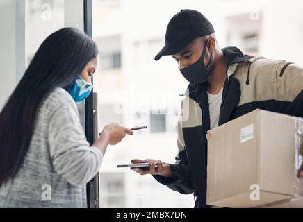 Une livraison sans contact permet à tout le monde de rester en sécurité. un jeune homme et une femme masqués utilisant un smartphone lors d'une livraison à domicile. Banque D'Images