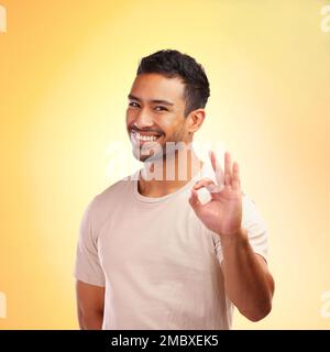 Portrait, mains et homme avec le signe ok en studio isolé sur fond jaune. Geste de la main, bon emoji et joyeux jeune homme modèle avec symbole pour Banque D'Images