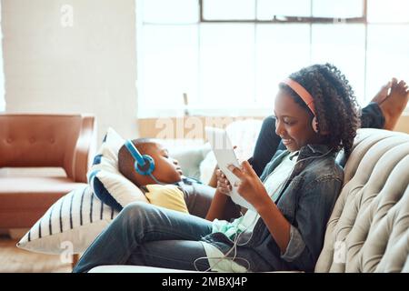 Une tablette et un casque pour se détendre sur un canapé dans le salon et profiter du divertissement ou du wi-fi à la maison. Une sœur et un frère heureux se détendent Banque D'Images