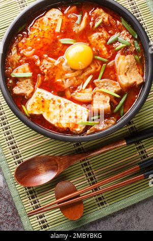 Le ragoût coréen classique Kimchi Soondubu jjigae présente du tofu siken dans un bouillon de kimchi flamboyant sur le bol de la table. Vue verticale du dessus de l'Abov Banque D'Images