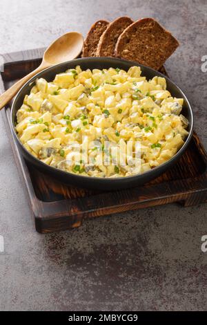 Salade allemande aux œufs avec pommes et cornichons vêtus de mayonnaise, vue rapprochée dans un bol sur la table. Verticale Banque D'Images