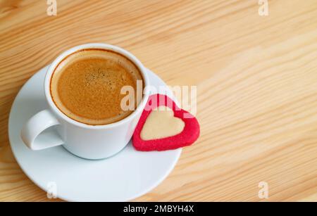 Une tasse de café chaud et mousseux avec un cookie en forme de cœur sur une table en bois Banque D'Images