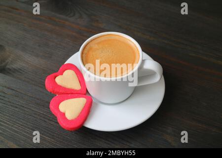 Tasse de café expresso avec une paire de biscuits en forme de cœur sur fond en bois noir Banque D'Images