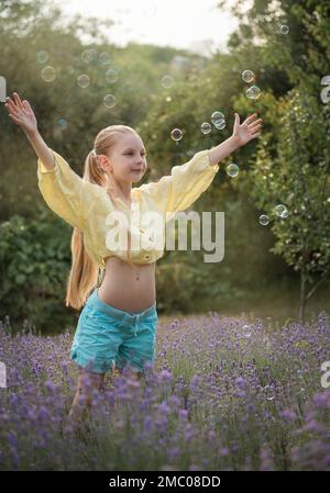 Belle petite fille attrape des bulles de savon dans un champ de lavande Banque D'Images