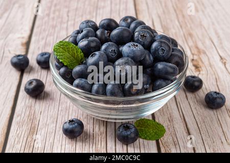 Bleuet mûr dans un bol en verre sur fond de bois. Bleuets frais pour le dessert végétarien. Baies sauvages pour un antioxydant naturel et une alimentation saine Banque D'Images