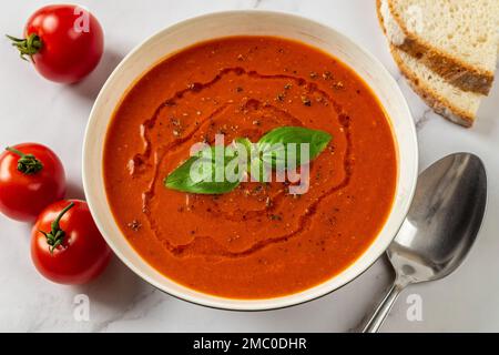 Soupe de tomates chaudes dans un bol blanc en gros plan. Plat de légumes frais de tomates en purée, ail et basilic prêts à manger. Plat végétarien sain. Banque D'Images