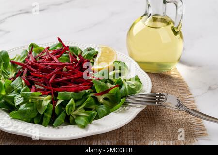 Salade de laitue agneaux avec betteraves crues en gros plan. Feuilles de salade de maïs vertes, betteraves crues râpées et fourchette sur une plaque blanche sur une surface en marbre. Aliments à faible teneur en calories. Banque D'Images