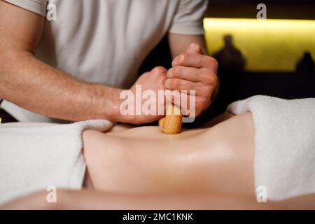 Gros plan les mains d'un grand masseur massent l'abdomen de la femme avec des bâtons de bambou Banque D'Images