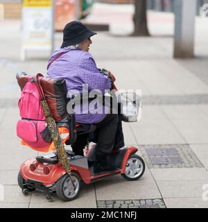 Femme âgée avec scooter électrique faisant des achats de fenêtre dans le centre-ville de Magdeburg, Allemagne Banque D'Images