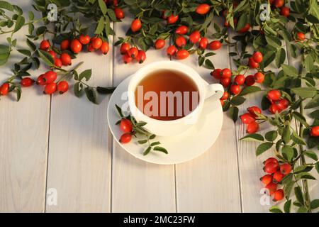 Tasse de thé avec baies de rose sur fond de bois blanc Banque D'Images