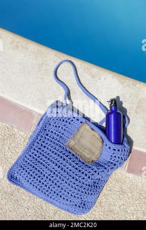 Bouteille bleue légère en aluminium réutilisable dans un sac fourre-tout à la main en crochet au bord de la piscine, mode de vie durable zéro déchet Banque D'Images