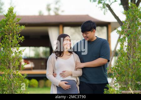 Femme enceinte asiatique avec son mari marchant ensemble dans le jardin à la maison pour se détendre et respirer de l'air frais. Banque D'Images