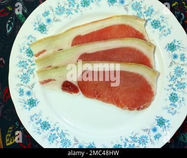 Trois tranches ou tranches de bacon cru sur une assiette prête à cuire. Banque D'Images