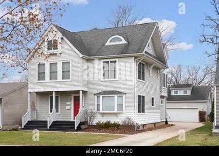 Une maison de banlieue grise de deux étages avec un porche couvert avec des balustrades blanches, et une porte d'entrée rouge. Banque D'Images