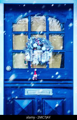 Couronne de Noël sur une porte avant bleue avec chute de neige Banque D'Images