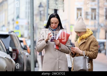 Personnes utilisant un smartphone dans la rue urbaine. Deux jeunes femmes dans des vêtements chauds avec des téléphones portables dans les mains Banque D'Images