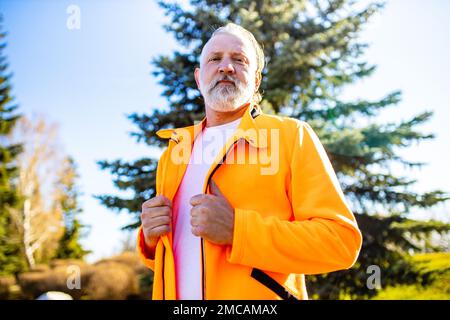 Homme âgé en orange sport porter s'étirant se réchauffer à l'extérieur jour ensoleillé dans la forêt seule Banque D'Images
