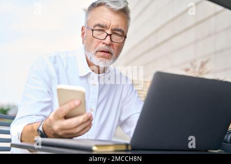 Homme d'affaires âgé utilisant un téléphone mobile travaillant sur un ordinateur portable à l'extérieur. Banque D'Images