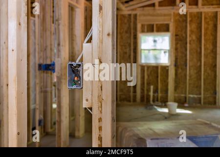 Une maison de cadre en bois non fini avec câblage électrique de base est en cours de construction sur un nouveau site de construction résidentielle Banque D'Images